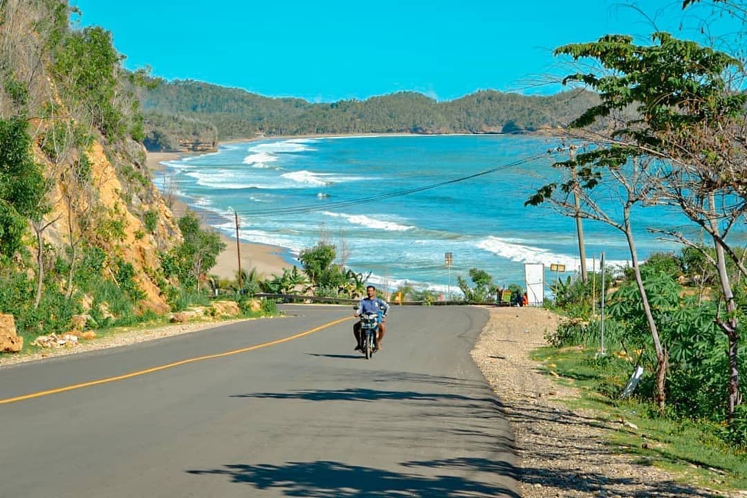 Seorang pengendara melintas di jalur menuju Pantai Soge Pacitan dengan latar ombak besar dan perbukitan hijau, Rabu, 26 November 2025. (Foto: Instagram @radikasepta)